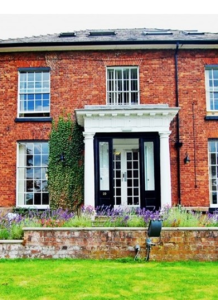 The front face of a large house with lawn in front.